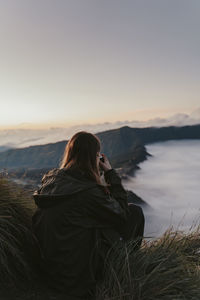 Rear view of woman on shore against sky during sunset