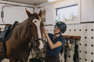 Woman in stable preparing horse for horse riding