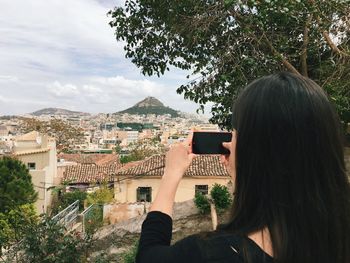 Rear view of woman photographing town through smart phone