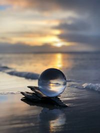 Close-up of crystal ball on beach against sky during sunset