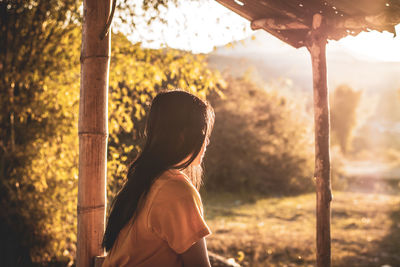 Rear view of woman standing by tree trunk