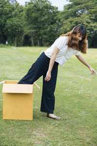 Full length of woman coming out of box on grass