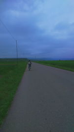 Road passing through field against cloudy sky