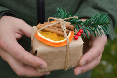 A man dressed  holding a present. gift is packed in craft paper with dried orange, cinnamon sticks