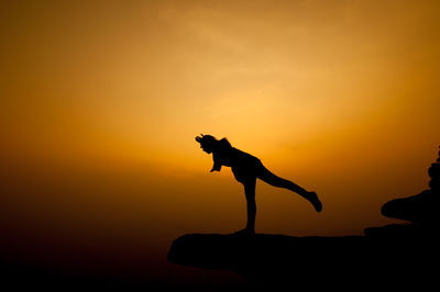 Silhouette woman standing on cliff against orange sky