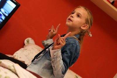 Thoughtful girl gesturing peace sign while sitting on bed at home