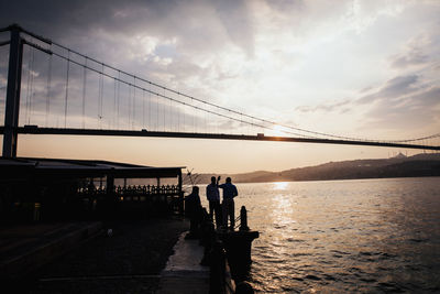 People on suspension bridge against sky during sunset