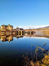 Reflection of buildings in lake against clear blue sky