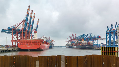 Cranes at harbor against sky