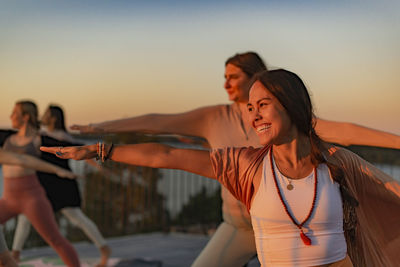 Happy woman doing yoga with female friend on patio at sunset