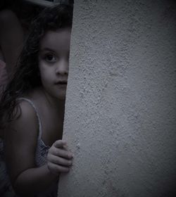 Girl looking away while standing by wall