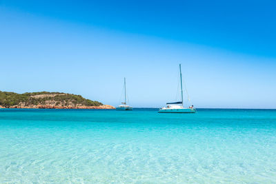 Sailboats sailing in sea against clear blue sky