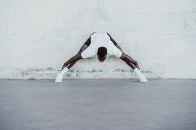 Young sportsman doing stretching exercise against white wall
