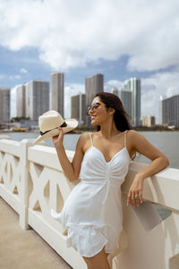 Young woman holding camera against sky