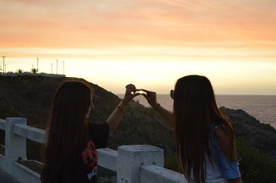 Rear view of woman photographing sea against sky during sunset