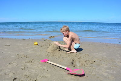 Full length of shirtless boy on beach against sky