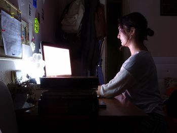 Woman using laptop while sitting in darkroom