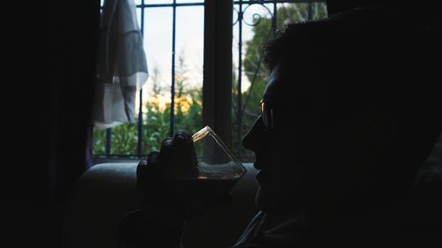 Close-up of man having wine by window at home