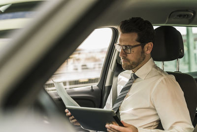 Successful businessman sitting in car using digital tablet