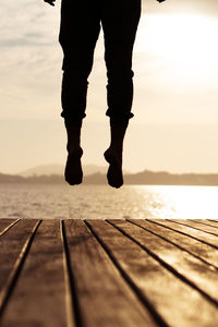Low section of man on pier over sea against sky jumping on a deck at the sunrise