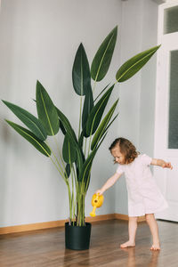 Little girl waters flowers at home, helps care for plants
