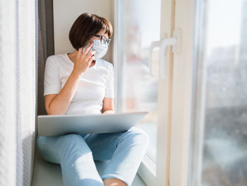 Woman in medical mask remote works with smartphone and laptop. coronavirus covid19. 