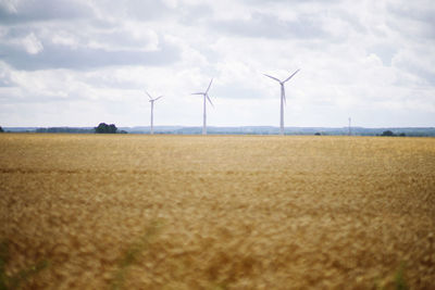 Wind turbines on field against sky