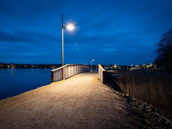 Illuminated pier over sea against sky at dusk