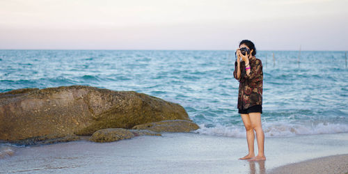 Young woman standing on rock at beach against sky