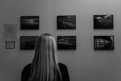 Rear view of blond woman looking at picture frames mounted on wall