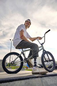 Bmx rider with prosthetic foot confidently posing on bike against cloudy sky at skateboard park