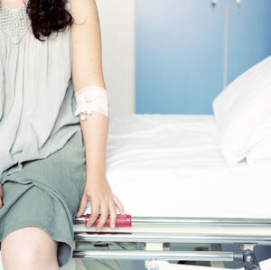 Midsection of mid adult woman sitting on bed at hospital