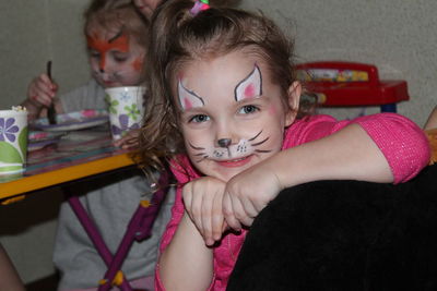 Portrait of girl with face paint while sitting on chair at home with sibling in background