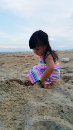 Baby girl playing with sand at beach against sky during sunset