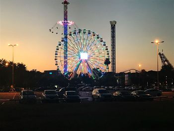 Illuminated ferris wheel against sky at sunset