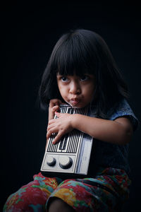 Portrait of cute girl sitting against black background