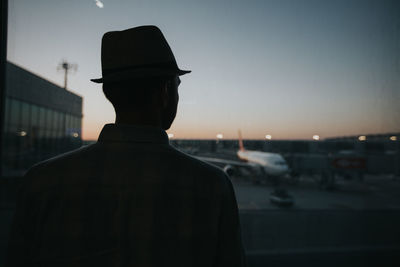 Rear view of silhouette man in city against sky during sunset