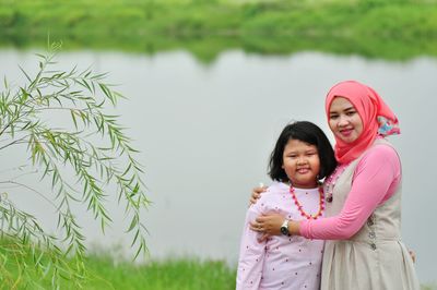 Portrait of smiling mid adult woman with daughter standing against lake