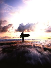 Silhouette man standing in sea against sky during sunset