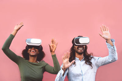 Couple looking through virtual reality simulator against pink background