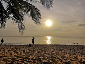 Silhouette people on beach against sky during sunset