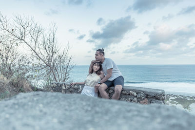 Couple embracing while sitting against sea and sky