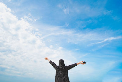 Low angle view of person with arms outstretched standing against blue sky