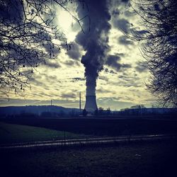 Bare trees on landscape against cloudy sky