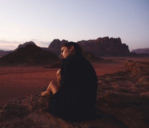 Woman sitting on rock in desert against clear sky