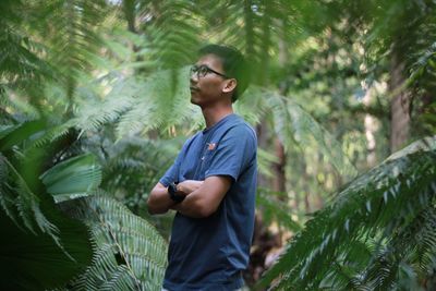 Man with arms crossed looking away while standing amidst forest