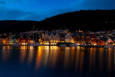 Illuminated buildings by river against sky at night