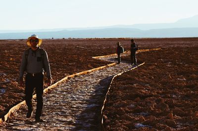 Full length portrait of man with friends walking on footpath in desert against sky