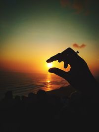 Silhouette hand holding sun over sea during sunset