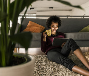 Smiling young woman at home holding cup and tablet